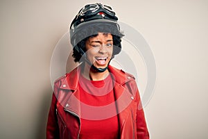 Young African American afro motorcyclist woman with curly hair wearing motorcycle helmet winking looking at the camera with sexy