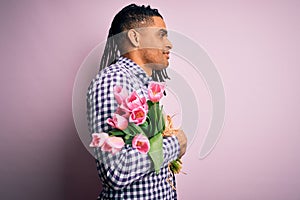 Young african american afro romantic man with dreadlocks holding bouquet of pink tulips looking to side, relax profile pose with