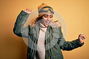 Young african american afro skier girl wearing snow sportswear and ski goggles Dancing happy and cheerful, smiling moving casual