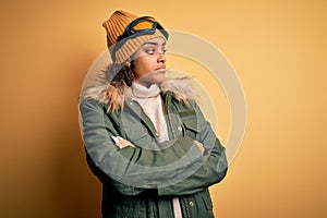 Young african american afro skier girl wearing snow sportswear and ski goggles looking to the side with arms crossed convinced and