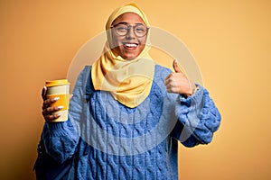 Young African American afro student woman wearing muslim hijab and glasses drinking coffee happy with big smile doing ok sign,