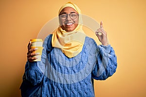 Young African American afro student woman wearing muslim hijab and glasses drinking coffee surprised with an idea or question