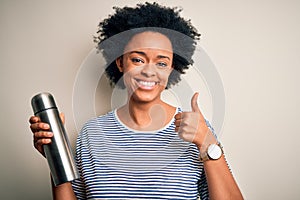 Young African American afro tourist woman with curly hair holding thermo with water happy with big smile doing ok sign, thumb up