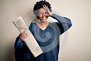 Young African American afro tourist woman with curly hair wearing backpack using city map with happy face smiling doing ok sign