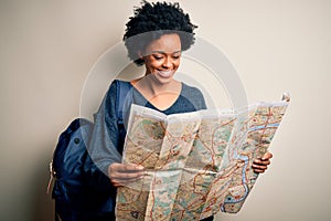 Young African American afro tourist woman with curly hair wearing backpack using city map with a happy face standing and smiling