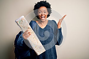 Young African American afro tourist woman with curly hair wearing backpack using city map very happy and excited, winner