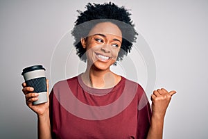 Young African American afro woman with curly hair drinking cup of coffee pointing and showing with thumb up to the side with happy