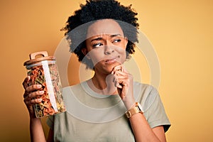 Young African American afro woman with curly hair holding bottle of dry Italian pasta serious face thinking about question, very