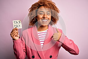Young African American afro woman with curly hair holding papaer with tax day message with surprise face pointing finger to