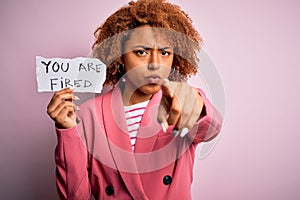 Young African American afro woman with curly hair holding papaer with you are fired message pointing with finger to the camera and