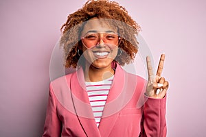 Young African American afro woman with curly hair wearing funny hearts sunglasses smiling with happy face winking at the camera