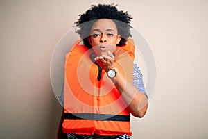 Young African American afro woman with curly hair wearing orange protection lifejacket looking at the camera blowing a kiss with