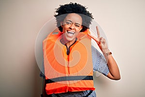 Young African American afro woman with curly hair wearing orange protection lifejacket smiling with happy face winking at the