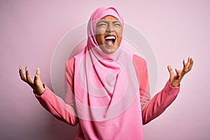 Young African American afro woman wearing muslim hijab over isolated pink background crazy and mad shouting and yelling with