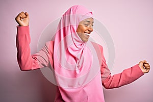 Young African American afro woman wearing muslim hijab over isolated pink background Dancing happy and cheerful, smiling moving