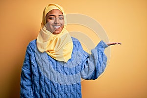 Young African American afro woman wearing muslim hijab over isolated yellow background smiling cheerful presenting and pointing