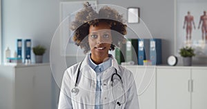 Young african-american-american female doctor putting stethoscope around neck standing in clinic office
