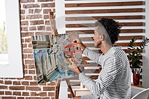 Young African-American artist painting picture in workshop