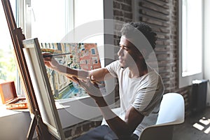 Young African-American artist painting picture in workshop