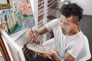 Young African-American artist painting picture in workshop