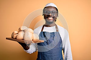 Young african american baker man wearing apron holding tray with homemade bread with a happy face standing and smiling with a