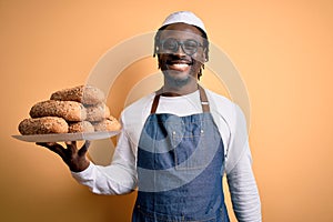 Young african american bakery man holding tray with healthy wholemeal bread with a happy face standing and smiling with a