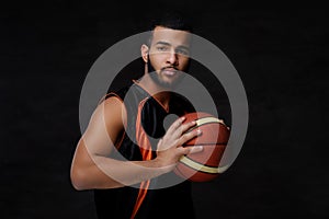 Young African-American basketball player in sportswear isolated over dark background.