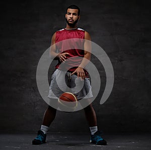 Young African-American basketball player in sportswear playing with ball. Isolated on a dark background.