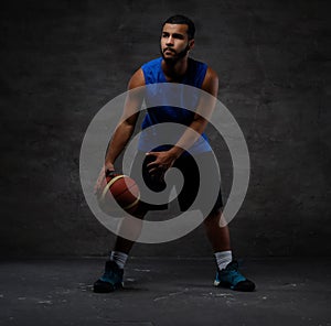Young African-American basketball player in sportswear playing with ball. Isolated on a dark background.