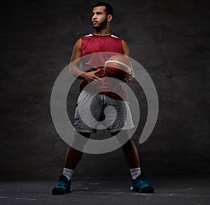 Young African-American basketball player in sportswear playing with ball. Isolated on a dark background.