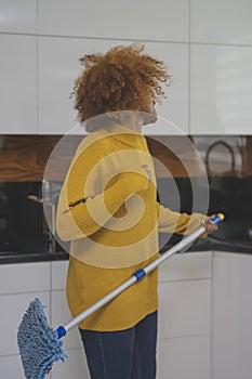 Young african american black happy woman using mop as guitar while cleaning the kitchen