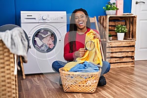 Young african american with braids holding magnifying glass looking for stain at clothes smiling and laughing hard out loud