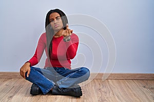 Young african american with braids sitting on the floor at home showing middle finger, impolite and rude fuck off expression