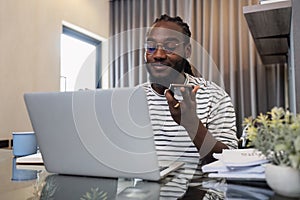 Young African American business man working with laptop and document on desk and talking on mobile at home