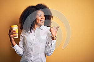 Young african american business woman with afro hair drinking coffee from take away cup pointing and showing with thumb up to the