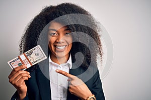 Young african american business woman with afro hair holding a bunch of cash dollars banknotes very happy pointing with hand and