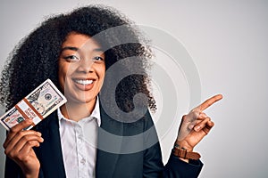 Young african american business woman with afro hair holding a bunch of cash dollars banknotes very happy pointing with hand and