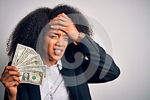 Young african american business woman with afro hair holding cash dollars banknotes stressed with hand on head, shocked with shame