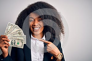 Young african american business woman with afro hair holding cash dollars banknotes very happy pointing with hand and finger