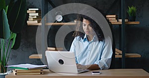 Young african american business woman with curly hair working on laptop computer, enjoying finishing work while sitting