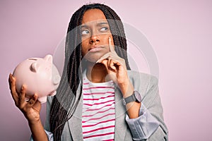 Young african american business woman saving money on piggy bank over  background serious face thinking about question,