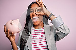 Young african american business woman saving money on piggy bank over isolated background with happy face smiling doing ok sign