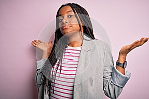 Young african american business woman standing over pink isolated background clueless and confused expression with arms and hands