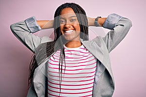 Young african american business woman standing over pink isolated background relaxing and stretching, arms and hands behind head