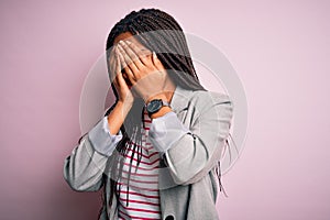 Young african american business woman standing over pink isolated background with sad expression covering face with hands while