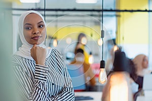 Young African American business woman standing  and smiling.  Happy successful business leader posing while her team in background