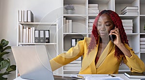 Young African American business woman talking on the phone and taking notes while working in the office