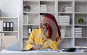 Young African American business woman talking on the phone and taking notes while working in the office