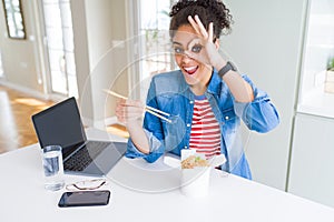 Young african american business woman working and eating asian noodles with happy face smiling doing ok sign with hand on eye