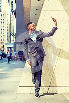 Young African American Businessman with beard, stretching arm, taking selfie on cell phone outside office in New York City